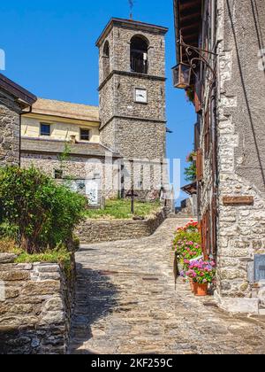 Cerreto Alpi, Reggio Apennin, Norditalien. Eine schmale Straße im alten Dorf mit der alten Pfarrkirche, die wie die Häuser aus Steinen gebaut wurde. Stockfoto