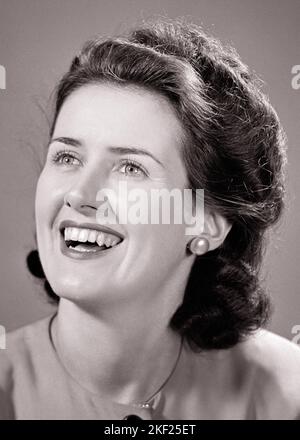 1940S PORTRAIT OF HAPPY SMILING BRUNETTE WOMAN LOOKING UP OFF CAMERA - G5218 HAR001 HARS OHRRING KOPF UND SCHULTERN FRÖHLICH AUFREGUNG FRISUR STOLZ LÄCHELT FRÖHLICH STYLISCH JUNGE ERWACHSENE FRAU SCHWARZ-WEISS KAUKASISCHE ETHNIE HAR001 ALTMODISCH Stockfoto