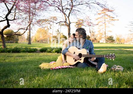 Verliebte Paare bei einem Picknick im Forest Park. Der Mann spielt eine Gitarre für seine Frau. Stockfoto