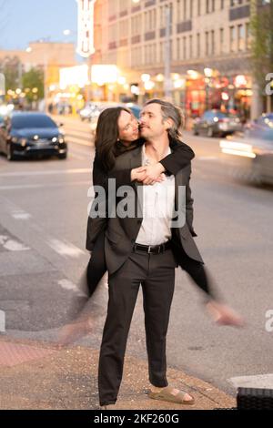 Romantische Fotos eines Paares, das in einer Innenstadt mit Straßenlaternen und Autos im Hintergrund für ein Date unterwegs war. Stockfoto