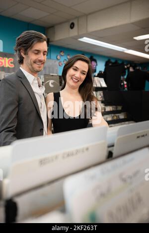 Ein Paar, das gemeinsam an einem Date in einem Vintage-Plattenladen stöbern, lachen und Spaß haben und nostalgische Musik ansehen. Stockfoto