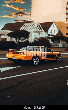 Eine orangefarbene Honda 2002 Acura NSX mit getönten Fenstern auf der Straße, mit Häusern und Gebäuden im Hintergrund Stockfoto