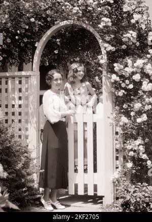 1930S LÄCHELNDE FRAU MUTTER UND MÄDCHEN TOCHTER STEHEN AM WEISSEN PFOSTENZAUN GARTENTOR IN DER UMGEBUNG BLÜHENDE ROSE ARBOR - J4733 HAR001 HARS ALTE MODE 1 JUVENILE STIL STREIKPOSTEN BEGRÜSSEN JUNGE ERWACHSENE FRIEDEN ROSE STARK ERFREUT FAMILIEN FREUDE ZUFRIEDENHEIT FRAUEN ROSEN GESUNDHEIT HEIM LEBEN LUXUS NATUR KOPIEREN RAUM FREUNDSCHAFT GANZKÖRPERFRAUEN TÖCHTER PERSONEN SZENISCHE INSPIRATION FÜRSORGLICHE GELASSENHEIT VERTRAUEN S&W SOMMERZEIT TOR TRÄUME GLÜCK FRÖHLICH UND ÄUSSERER STOLZ LÄCHELT ARBOR MUTTER UND TOCHTER MÜTTER UND TÖCHTER VERBINDUNG KONZEPTIONELLE FREUDIGE STREIKZAUN STILVOLLER ZAUBER Stockfoto