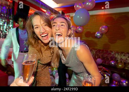 Porträt von zwei fröhlichen weißen Freundinnen, die lachen und Champagner in einem Nachtclub trinken Stockfoto