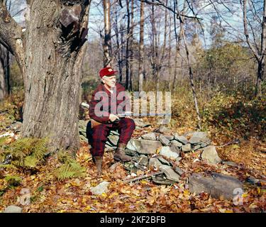 1970S 1980S ÄLTERER MANN, DER AUF EINEM STEINZAUN IM WALD SITZT UND ROTE SCHWARZE WOLLKLEIDUNG MIT DOPPELTEM FASS TRÄGT SCHROTFLINTE - KG4898 SHE001 HARS LIFESTYLE ZUFRIEDENHEIT ÄLTERE LÄNDLICHE NATUR WOLLE KOPIERER PLATZ IN VOLLER LÄNGE PERSONEN TRADITIONELLE MÄNNER RISIKO HUNTER KARO VERTRAUEN SENIOR MANN SENIOR ERWACHSENER JAGD FREIHEIT ZIELE GLÜCK ALTER OLDSTERS HIGH-ANGLE OLDSTER ABENTEUER FREIZEIT ERHOLUNG HERBST SAISON IN ON ELDERS STILVOLLE FEUERWAFFEN JÄGER HERBSTLICHE KAUKASISCHE ETHNIE DOPPELFASS FALLEN LAUB ALTMODISCH Stockfoto