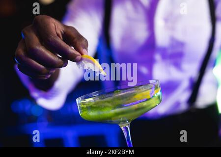 Der mittlere Teil des afroamerikanischen Barkeepers bereitet einen grünen Cocktail an einer Bar zu Stockfoto