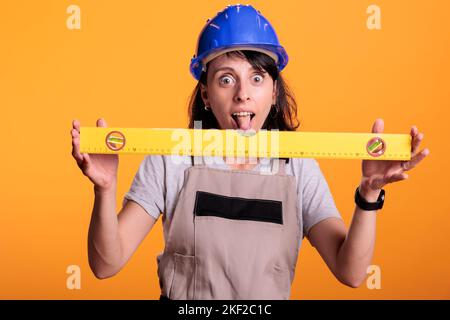 Fröhlicher Bauarbeiter, der Flachwände mithilfe einer Richtmaschine überprüft, am Gebäude arbeitet und im Studio die Renovierungsarbeiten abarbeitet. Frau Renoviererin Messung sogar Oberfläche mit Wasserstand Werkzeug, Zimmermann Arbeit. Stockfoto