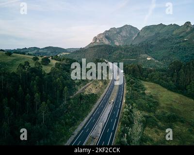 autobahn aus der Luft von einer Drohne ohne Verkehr gesehen einsam zwischen der Vegetation das Gras und die Bäume des Waldes in der Nähe der Berge Stockfoto