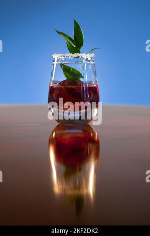 Rotes Getränk serviert mit grünem Blatt in einem garnierten Glas. Stockfoto