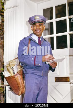 1960S PORTRAIT LÄCHELNDER AFROAMERIKANISCHER POSTBOTE, DER DIE POST VOR DER TÜR STEHEND IN POSTUNIFORM AUF DIE KAMERA SCHAUTE - KP1087 HAR001 HARS KOPIEREN RAUM HALBE LÄNGE PERSONEN POST MÄNNER MITTLEREN ALTERS MANN LIEFERN BLICKKONTAKT GESCHICKLICHKEIT BERUF GLÜCK FÄHIGKEITEN FRÖHLICHEN KUNDENSERVICE AFRO-AMERIKANER AFRO-AMERIKANISCHE SCHWARZE ETHNISCHE ZUGEHÖRIGKEIT ARBEIT STOLZ BESCHÄFTIGUNG BERUFE LÄCHELT POSTSENDUNG FREUDIGE POSTTASCHE VOR DER TÜR MITARBEITER USPS BEAMTER VEREINT STATES POSTAL SERVICE HAR001 ARBEITEN ALTMODISCHE AFROAMERIKANER Stockfoto