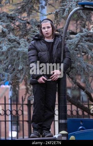 Während der Pause an seiner Yeshiva steht ein orthodoxer jüdischer Junge mit Peyot auf dem Sobel Playground in Brooklyn, New York. Stockfoto