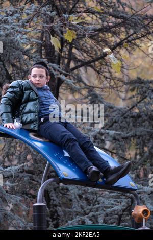 Ein orthodoxer jüdischer Junge sitzt während der Schulpause auf einem Klettergebiet. Auf dem Sobel Playground in Brooklyn, New York. Stockfoto