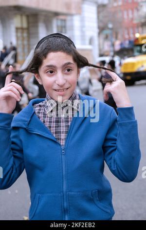 Ein junger chassidischer jüdischer Junge kräuselt seinen Peyot. In Brooklyn, New York City. Er erfüllt eine Mizwa mit besonderer Aufmerksamkeit. Stockfoto