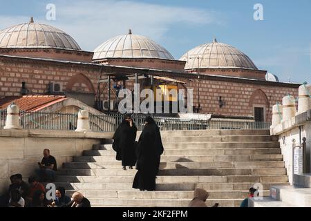 Istanbul, Türkei - 1 2022. Oktober: Fromme muslimische Frauen in traditionellen schwarzen Burkas treffen sich auf Stufen vor einer Moschee in Istanbul, Türkei. Stockfoto