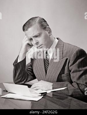 1940S NACHDENKLICHER MANN IN NADELSTREIFENANZUG, DER EIN RECHNUNGSSCHECKBUCH MIT STIFT AUF DER REZEPTION ÜBERPRÜFT UND AUF DIE ENTSCHEIDUNG WARTET, ZU ZAHLEN - S11336 HAR001 HARS BETROFFENE TRAURIGKEIT ANZUG UND KRAWATTE WAHL REFLEKTIERENDE THINK GELEGENHEIT STIMMUNGSBERUFE REFLEKTIERENDE NACHDENKER ERWÄGEN VERLOREN IN GEDANKEN GLUM STILVOLLE KONTEMPLATIVE MEDITIEREN KONE MEDITATIVE MID-ADULT MID-ADULT MANN MISERABLE LÖSUNGEN SCHWARZ-WEISS KAUKASISCHEN ETHNIE UNTER BERÜCKSICHTIGUNG HAR001 ALTMODISCH Stockfoto