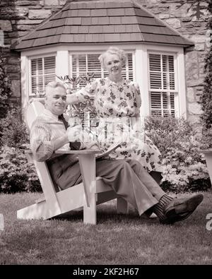 1940S PORTRAIT SENIOR PÄRCHEN SITZT ADIRONDACK STIL STUHL AUF DER VORDERSEITE RASEN STEIN HAUS MIT BAY FENSTER LÄCHELND BLICK AUF DIE KAMERA - S9435 HAR001 HARS DESIGN FREUDE FREUDE LIFESTYLE ZUFRIEDENHEIT ARCHITEKTUR ÄLTERE HÄUSER PIPE BAY GESUNDHEIT HEIM LEBEN LUXUS KOPIE RAUM FREUNDSCHAFT HALBLANGE WOHNGEBÄUDE RUHESTANDSVERTRAUEN ÄLTERER MANN ÄLTERER ERWACHSENER ADIRONDACK MITTLEREN ALTERS B & W MITTLEREN ALTERS MANN ÄLTERE FRAU ERFOLG RENTNERSTRUKTUR GLÜCK IM ALTER FRAU IM MITTLEREN ALTER OLDSTERS FRÖHLICH OLDSTER FREIZEIT ÄUSSERER STOLZ HÄUSER LÄCHELT ÄLTESTEN FREUDIGE RESIDENZ STILVOLLE ZUSAMMENARBEIT ZWEISAMKEIT Stockfoto
