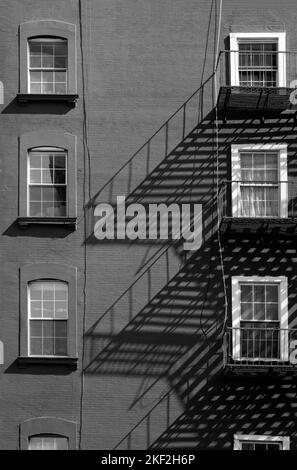 Der Schatten eines Feuers entweicht an der Wand eines kleinen Mehrfamilienhauses an der 10. Avenue und der West 23. Street im Stadtteil Chelsea in New York City. Stockfoto