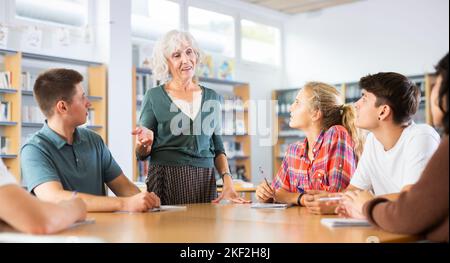 Ältere Lehrer, zusammen mit Jugendlichen Studenten, führt Tischklassen in der Schulbibliothek Stockfoto