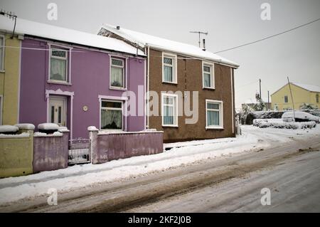 Winterszene in Merthyr Tydfil. Farbenfrohe Häuser im Schnee mit einem silbernen Himmel im Hintergrund. Stockfoto