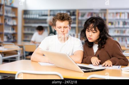 Asiatische Schülerin mit Klassenkamerad Kerl, studieren auf einem Laptop und Notizen in einem Copybook Stockfoto