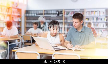 Asiatische Schülerin mit Klassenkamerad Kerl, studieren auf einem Laptop und Notizen in einem Copybook Stockfoto