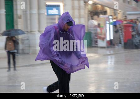 Valletta, Malta - 12. November 2022: Ein Mann mit purpurfarbenem Notregen-Poncho läuft, um sich vor dem fallenden Regen zu verstecken, in Bewegung verschwommen Stockfoto