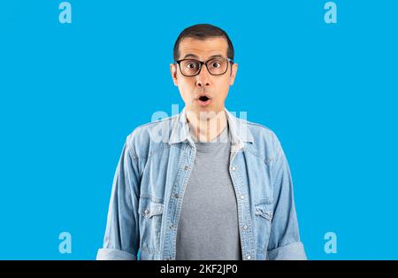 Studioaufnahme eines hispanischen Mannes, der eine Brille auf einem isolierten blauen Hintergrund trägt, ängstlich und schockiert mit überraschenden Gesichtsausdrücken, Angst und aufgeregt. Stockfoto