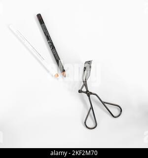 Brauner Lippenstift, weißer Eyeliner-Bleistift und Wimpern-Lockenstab auf weißem Hintergrund; Lippen- und Augen-Make-up und Kosmetik. Stockfoto