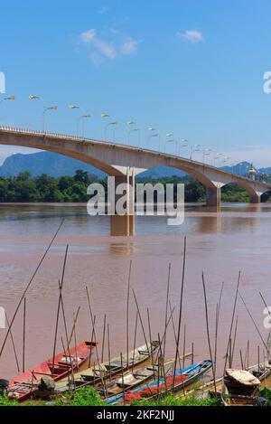 Mekong-Flussboote und die Freundschaftsbrücke, die von Thailand nach Laos führt, mit Bergen in der Ferne. Stockfoto