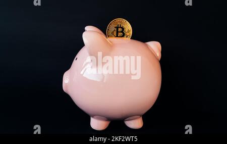 Kryptowährungs-Sparschwein-Finanzbankkonzept auf schwarzem Hintergrund. Krypto-Bitcoin-Münze in Ersparnisse gesteckt Stockfoto