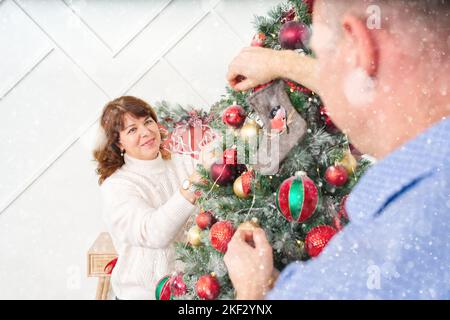Lächelndes, glückliches Paar im mittleren Alter, das Weihnachtsbaum zu Hause schmückt. Glückliches Paar zusammen zu Hause, weihnachtskonzept Stockfoto