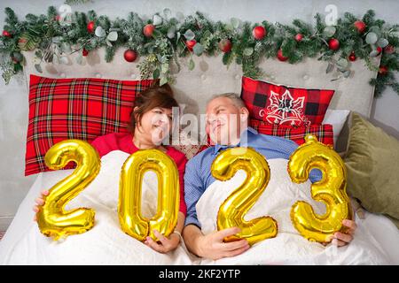 Schönes Paar liegt im Bett und plant, ein Baby zu haben. Weihnachten und frohe Neujahr mit den Zahlen 2023 Stockfoto