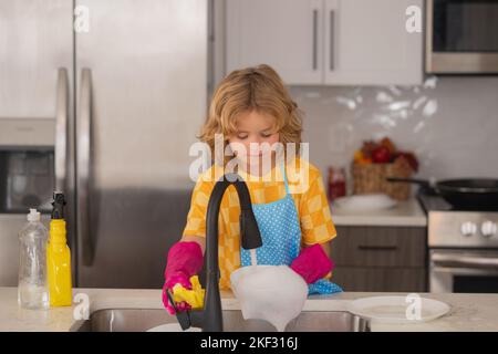 Kinder waschen Geschirr in der Küche. Kind hilft bei der Hausarbeit. Housekeeping- und Hausreinigungskonzept. Reinigen Sie das abgewaschene Geschirr, das Spülen Stockfoto