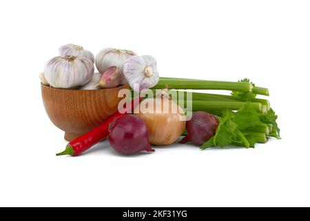 Zwiebeln, Chili und Knoblauchzwiebeln in Holzschüssel vor frischem Sellerie-Stiel, Gewürzen oder Gewürzmotiven Stillleben isoliert auf weißem Hintergrund Stockfoto