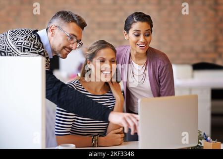 Ich denke, ich mag diese am meisten. Ein reifer Mann, der einer Arbeitskollegin auf ihrem Laptop im Büro hilft. Stockfoto