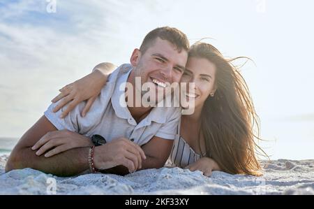 Porträt, Liebe und Entspannung Paar, Strand und Urlaub im Sommer Sonnenuntergang. Glückliche Frau umarmt ihren fröhlichen Mann, während sie im Urlaub oder im Sand am Meer liegt Stockfoto