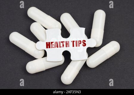 Medizinkonzept. Auf schwarzem Hintergrund, Kapseln und ein Puzzle mit der Aufschrift - GESUNDHEITSTIPPS Stockfoto