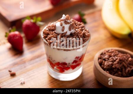 Gesundes Frühstück mit griechischem Joghurt mit frischem Obst und Puffreis mit Schokoladengeschmack auf einem rustikalen Holztisch. Stockfoto