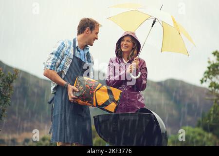 Der Regen hält mein Grillen nicht auf. Ein Paar grillen glücklich im Regen. Stockfoto