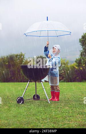 Schutz des Grills vor dem Wetter. Ganzkörperaufnahme eines Jungen, der im Regen vor einem Grill im Freien steht. Stockfoto