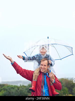 Regenwetter ist unser Lieblingswetter. Ein Vater trägt seinen Sohn auf den Schultern draußen im Regen. Stockfoto