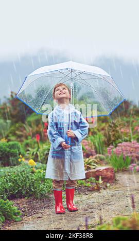 Mein Garten liebt den Regen. Ganzkörperaufnahme eines Jungen, der draußen im Regen steht. Stockfoto