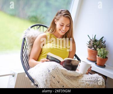 Vertieft in die Fantasie ihres Romans. Eine junge Frau, die zu Hause ein Buch liest. Stockfoto