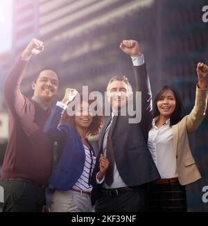 Erfolg ist das, worum es uns geht. Ein motiviertes Business-Team, das seine Hände für den Erfolg hochlegt, während es draußen steht. Stockfoto