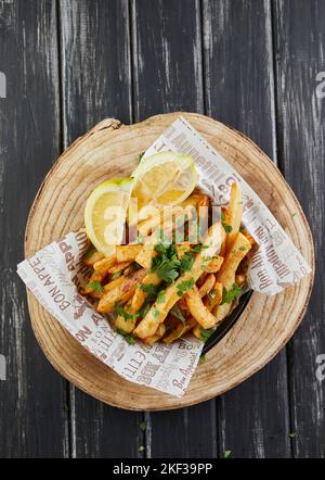 Kartoffeln mit Petersilie und Zitrone, in Öl auf Holzbrett gebraten, im Café servieren Stockfoto