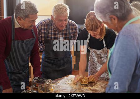Zeigt ihnen, wie man in wenigen Minuten Mahlzeiten zubereitet. Eine Gruppe von Senioren, die an einem Kochkurs teilnehmen. Stockfoto