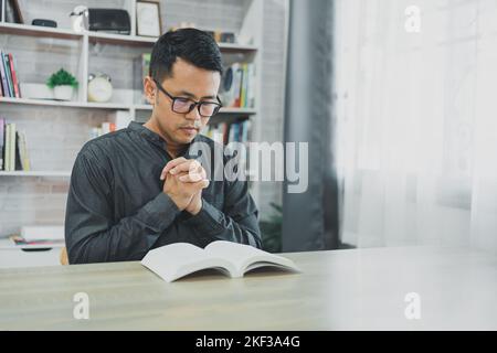 Asiatischer Mann, der im Gebet zu Gott die Hände zusammen tut Zusammen mit der bibel im christlichen Konzept von Glauben, Spiritualität und Religion beten Männer in der Bibel Stockfoto