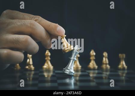 Geschäftsmann Hand bewegt Gold Schach König Figur und Schachmatt Gegner während Schachbrett Wettbewerb. Entscheidungsziel, Erfolg, Management, b Stockfoto