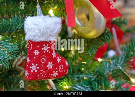 Roter Weihnachtsstrumpf für Geschenke auf einem Weihnachtsbaum mit Spielzeug und Girlanden. Stockfoto