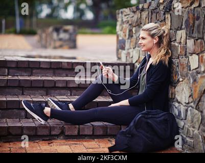 Musik motiviert sie. Eine sportliche junge Frau, die draußen Musik hört. Stockfoto